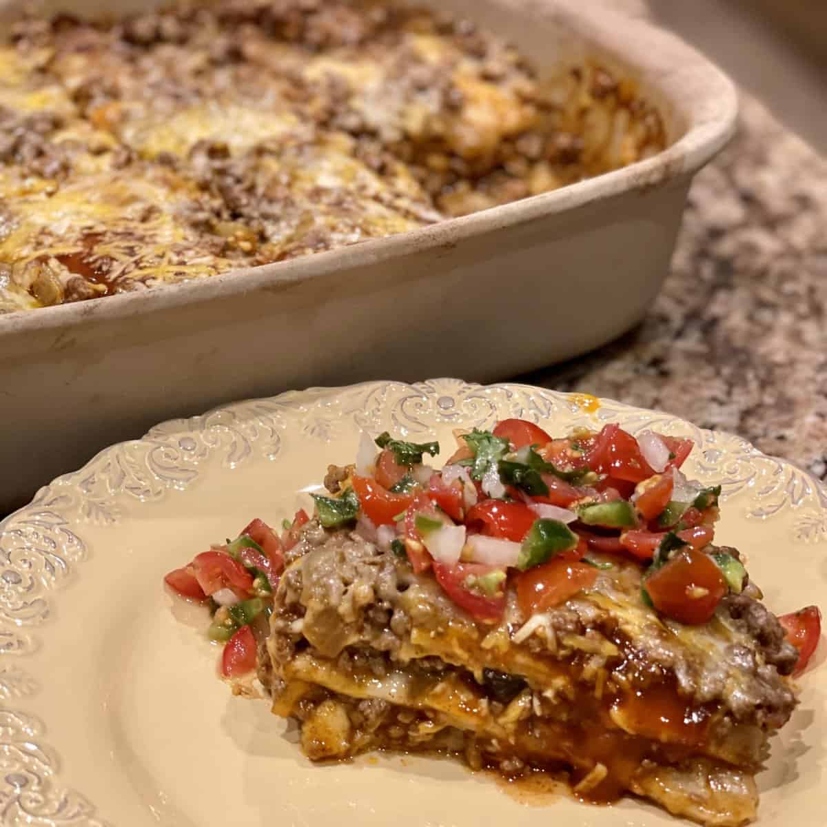 A slice of taco lasagna on a plate with pico on top.