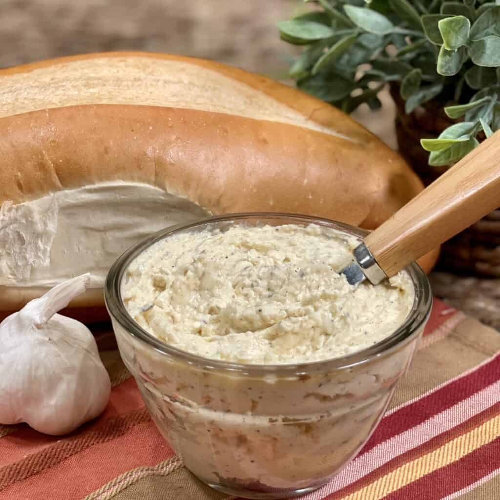 Garlic butter in a bowl next to a loaf of bread.