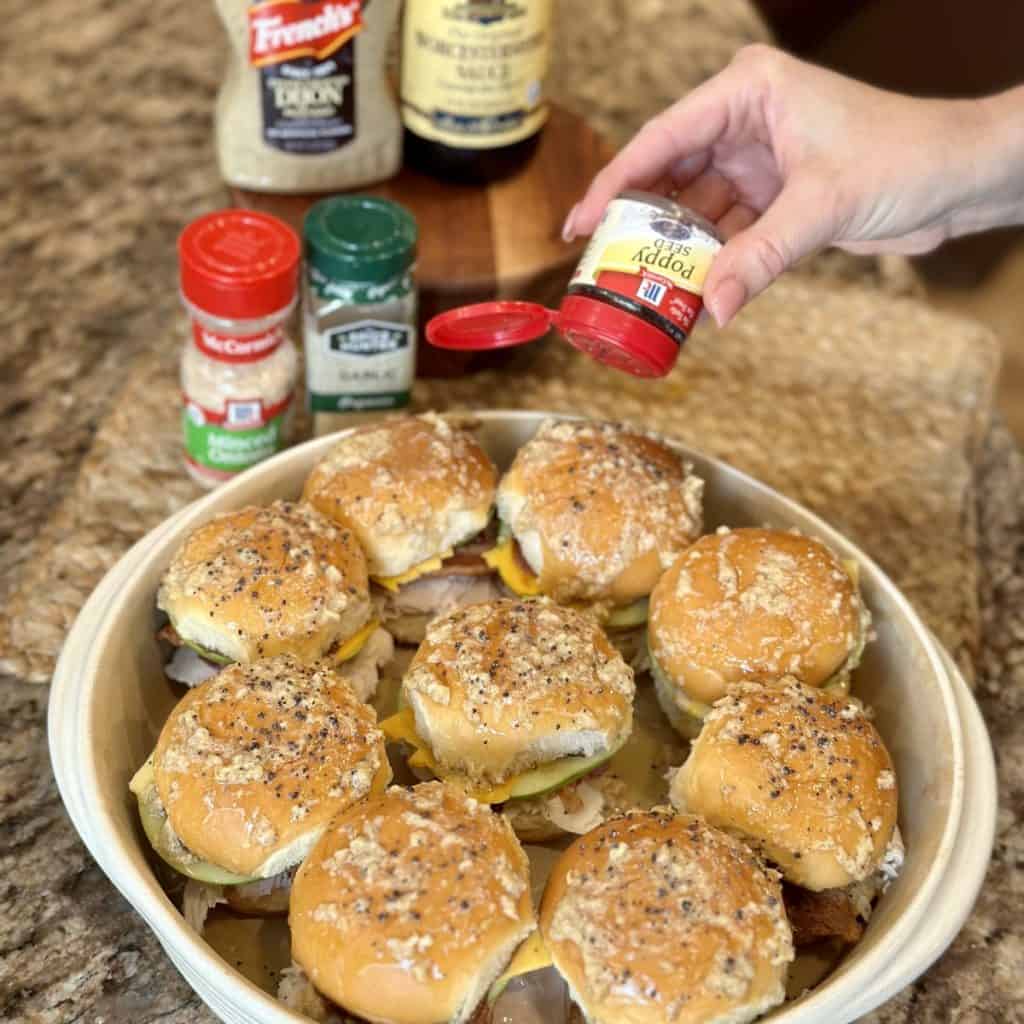 Sprinkling poppy seeds on top of sliders.