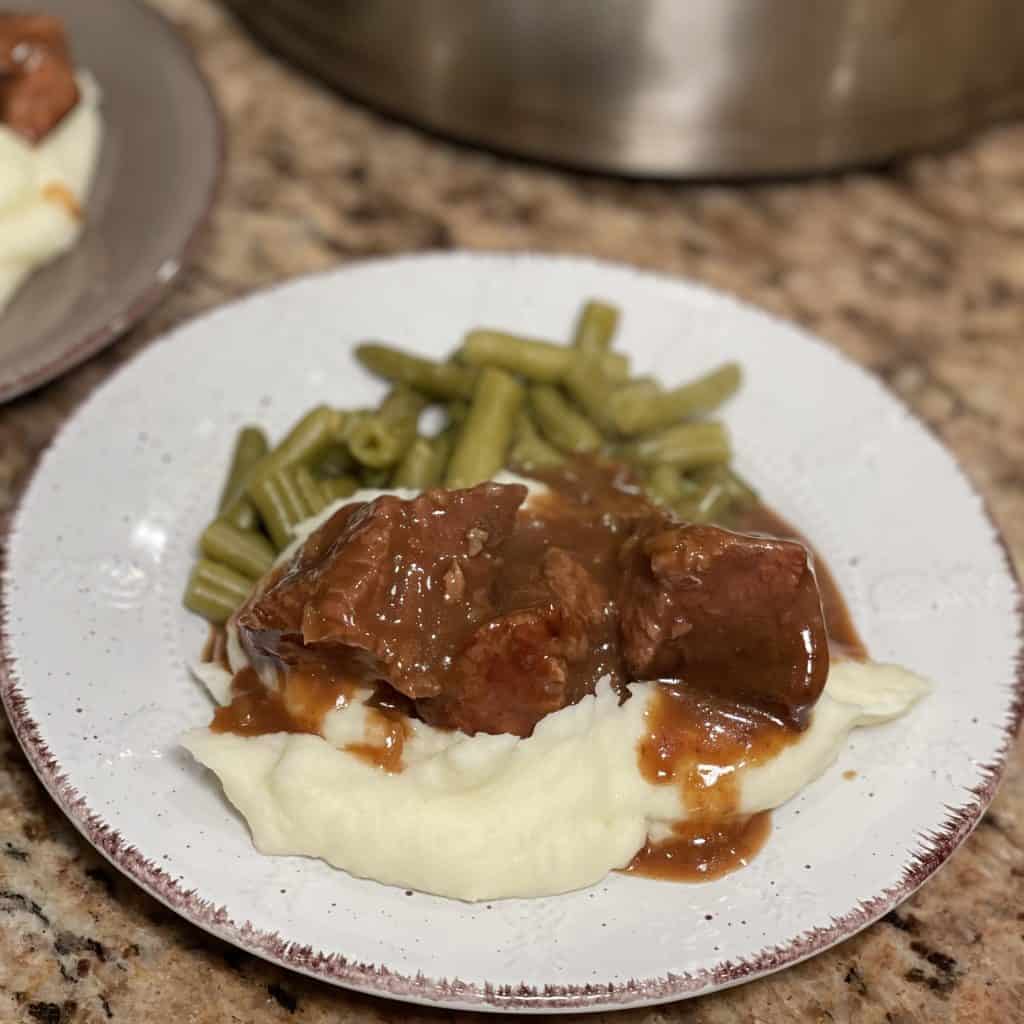 This is a picture of a dinner plate topped with mashed potatoes, beef and brown gravy.