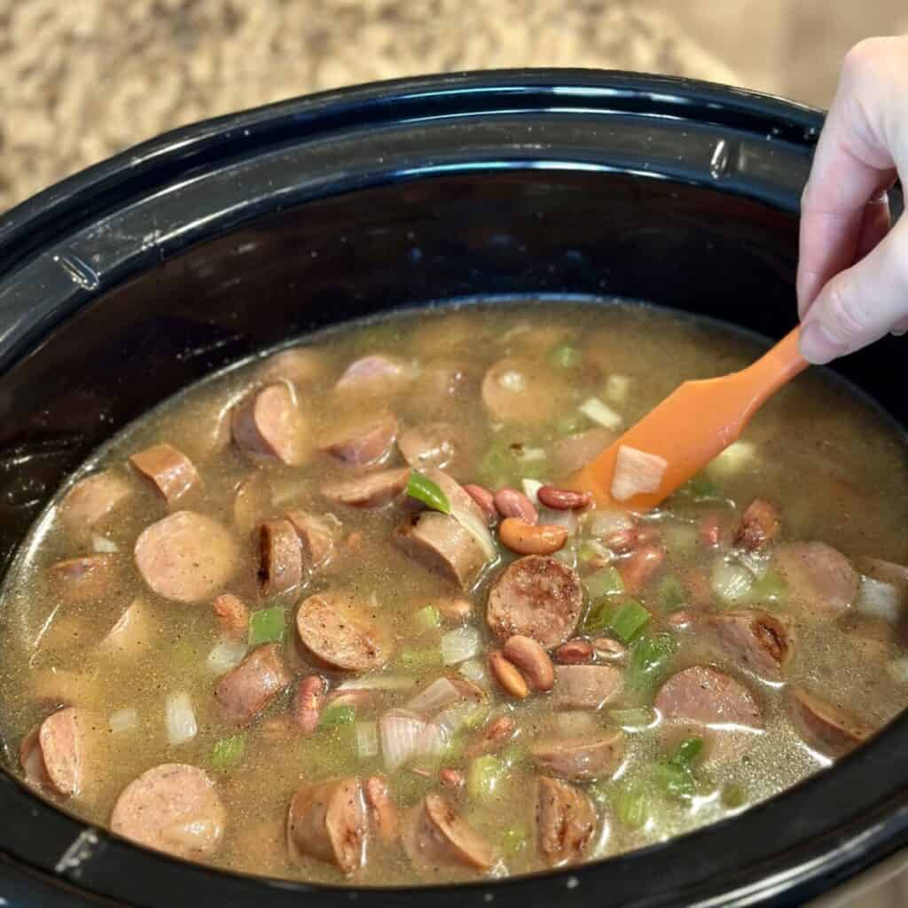 Mixing ingredients together in a crockpot for red beans and rice.