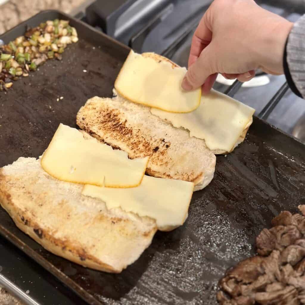 Adding cheese slices to bread on a griddle.
