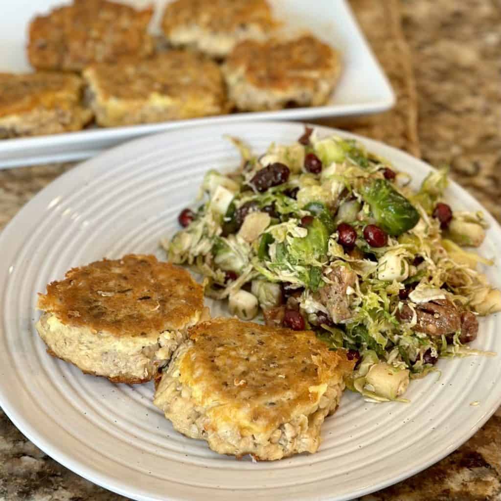 A plate with 2 salmon patties and salad on top.