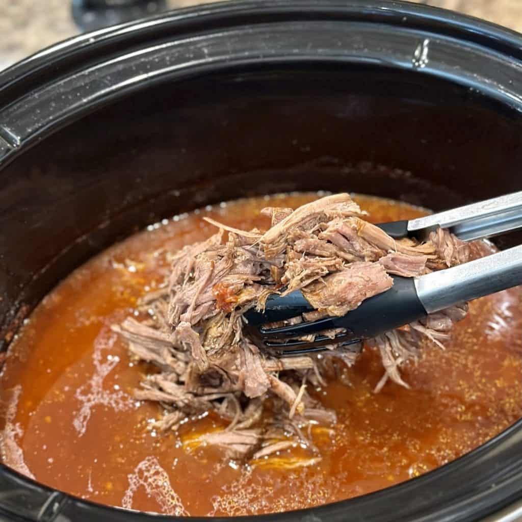 Adding cooked shredded beef back to a crockpot.