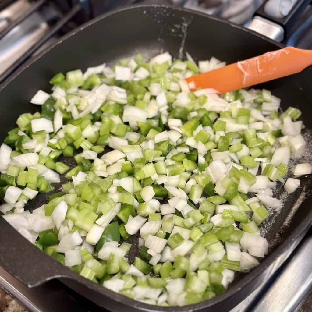 Sautéing the holy trinity, celery, onion and green pepper, in a skillet.