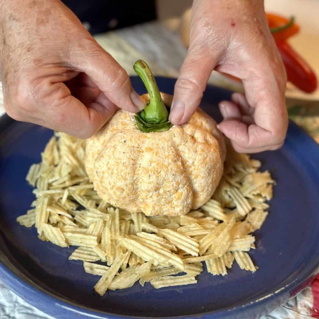 Pressing a bell pepper stem in a cheeseball to look like a pumpkin.