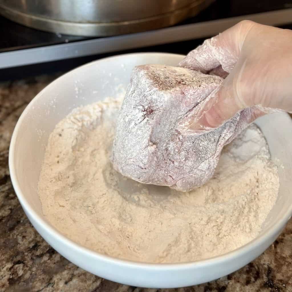 Dredging a beef seasoned beef rib in flour.