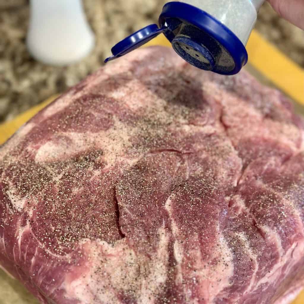 Seasoning a pork butt with salt and pepper.