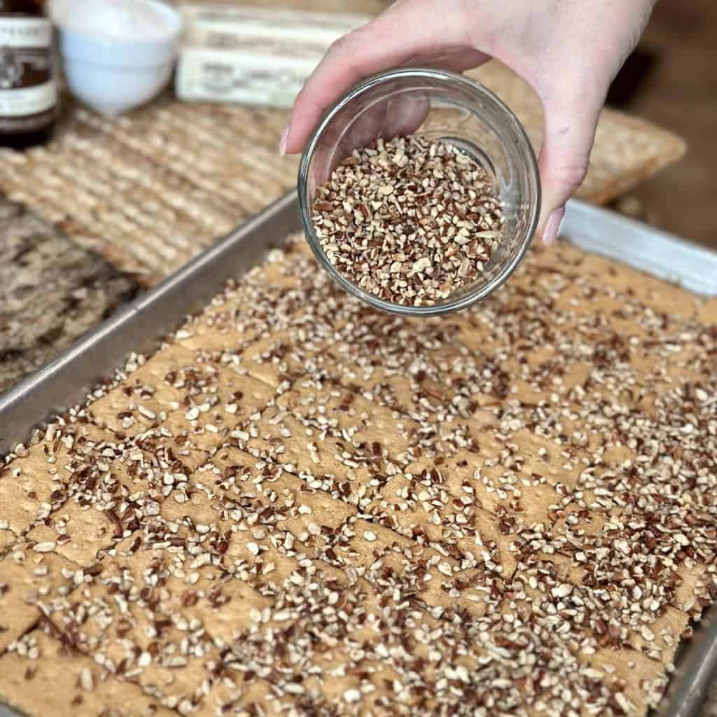 Sprinkling pecans on graham crackers on a sheet pan.