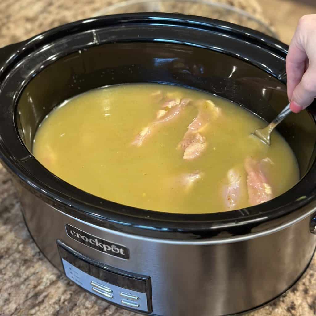 chicken submerged in the enchilada sauce and broth in a crockpot