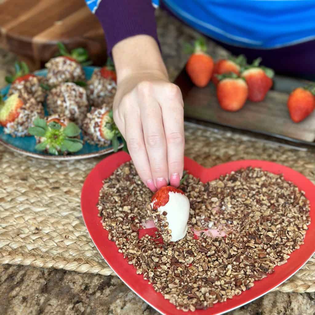 cream cheese coated strawberry being rolled in chopped pecans