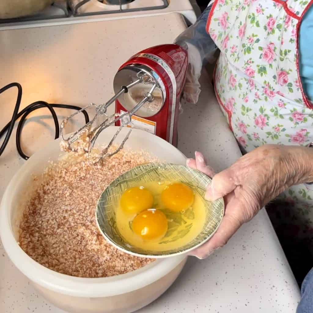 Adding eggs to a jam cake batter.