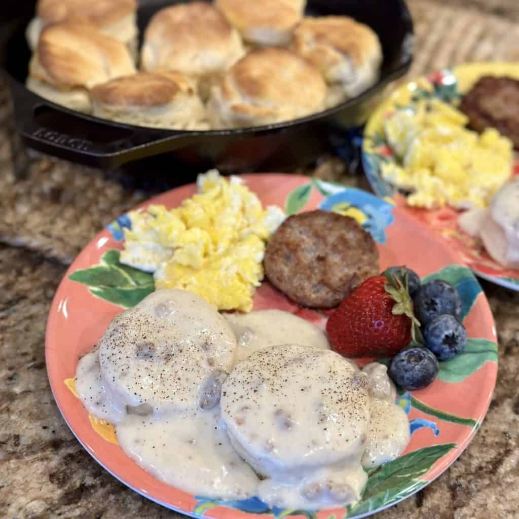A plate of biscuit and gravy, sausage, egg, and fruit.