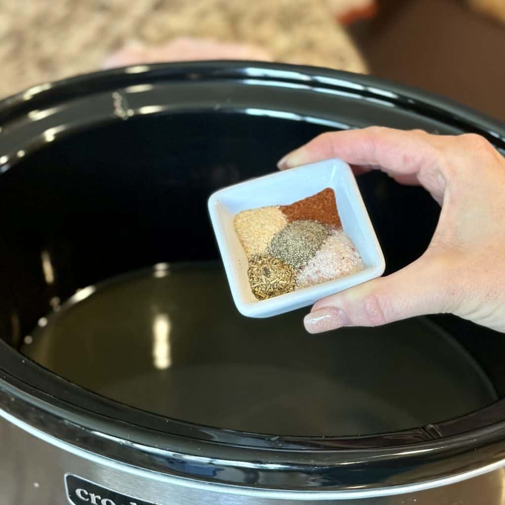 Adding seasonings to a crockpot filled with broth.