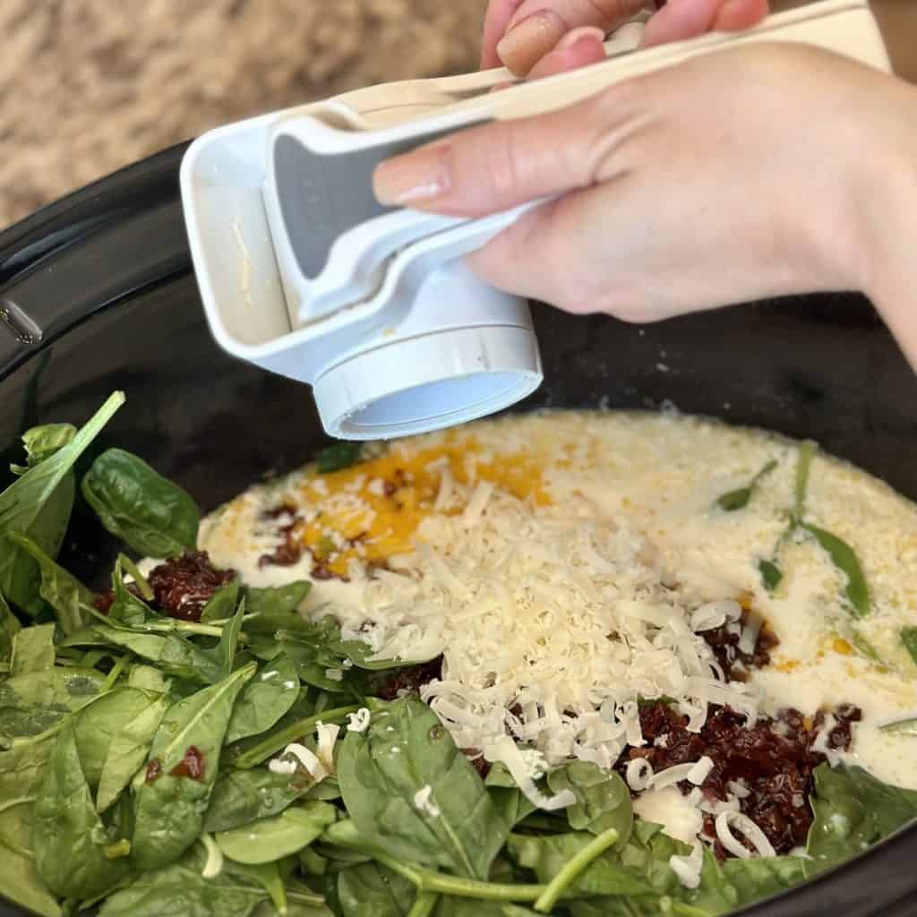 Adding parmesan cheese to a crockpot meal of chicken and spinach.
