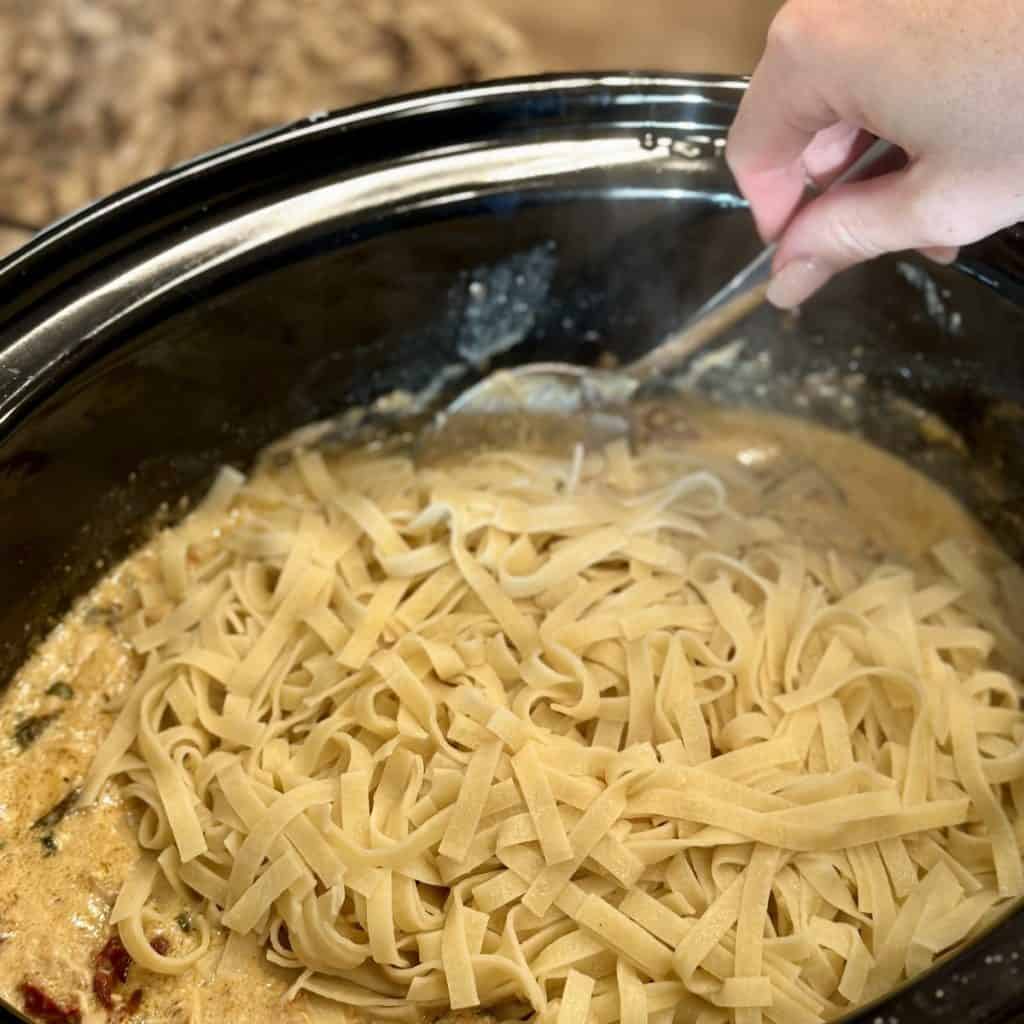 Mixing pasta into the crockpot of Tuscan chicken.
