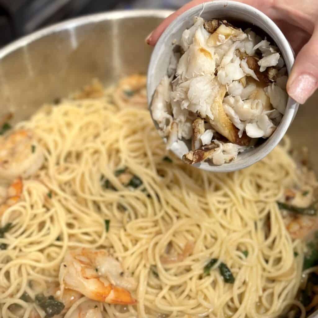 Adding crab to pasta in a pan.