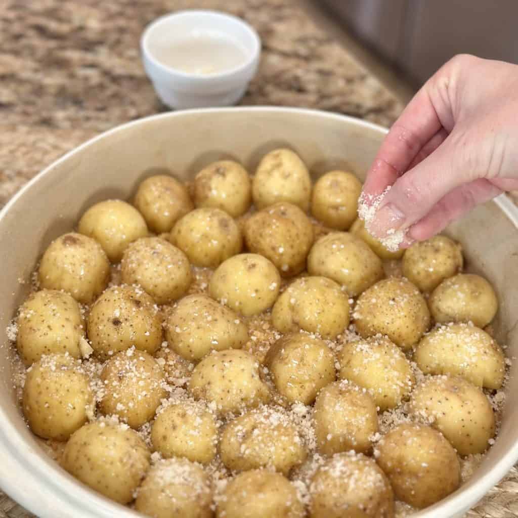 Sprinkling cheese on potatoes in a baking dish.