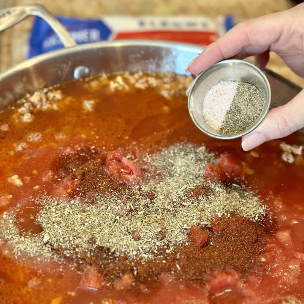 Adding seasonings to a pot of tomato sauce and ground beef.