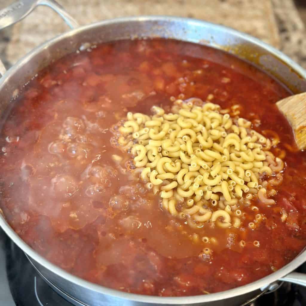 Adding elbow macaroni to a pot of goulash.