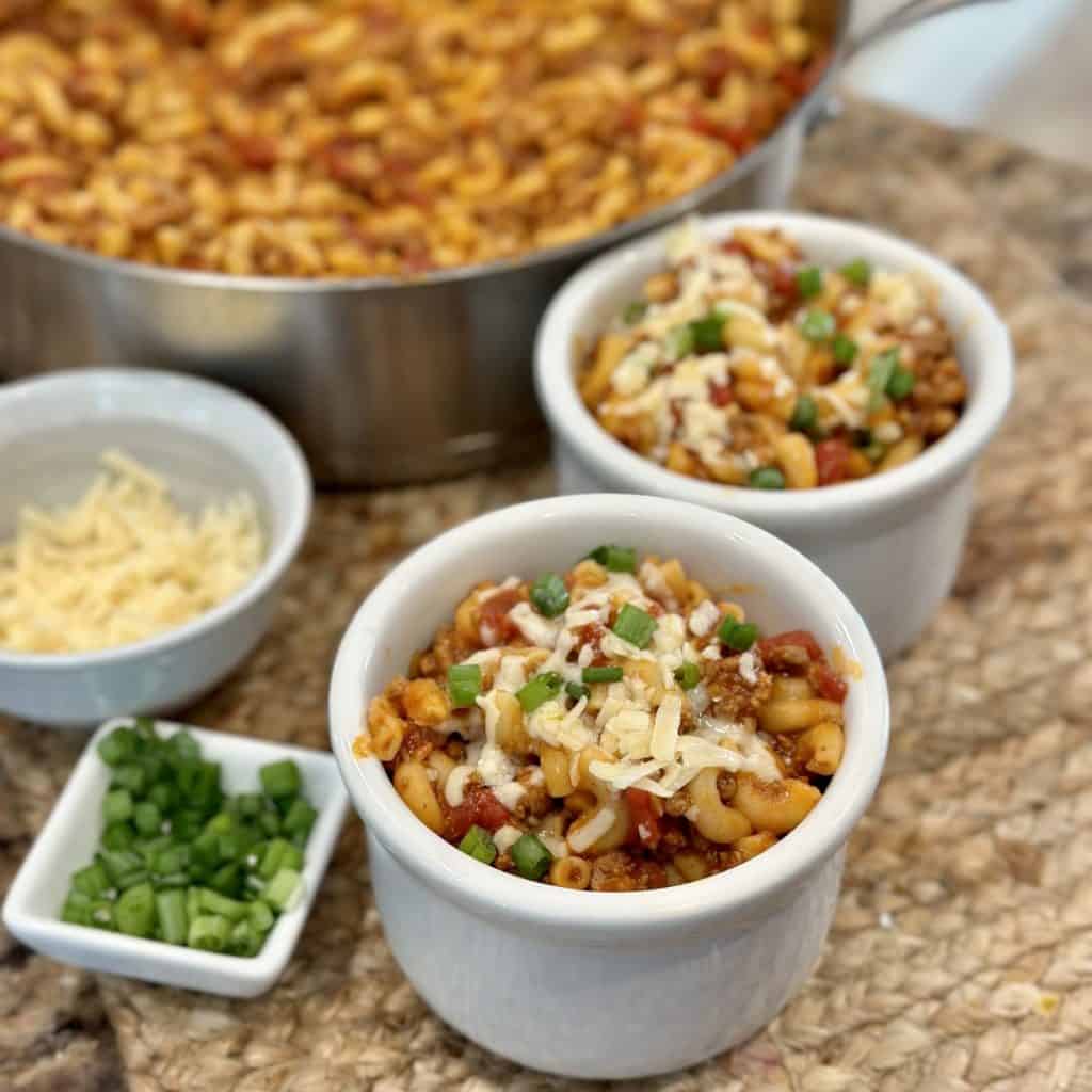 Bowls of beef goulash with cheese and green onion on top.