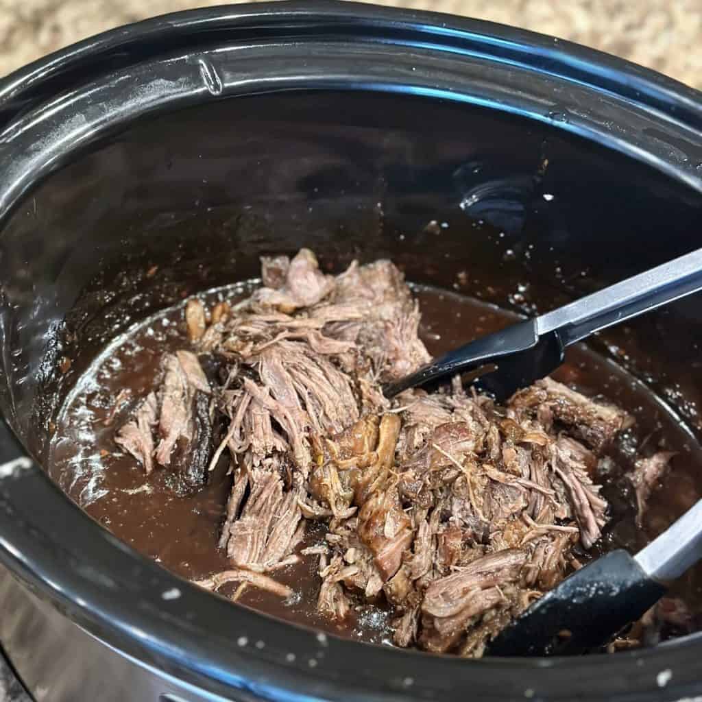Adding shredded cooked beef to a crockpot.