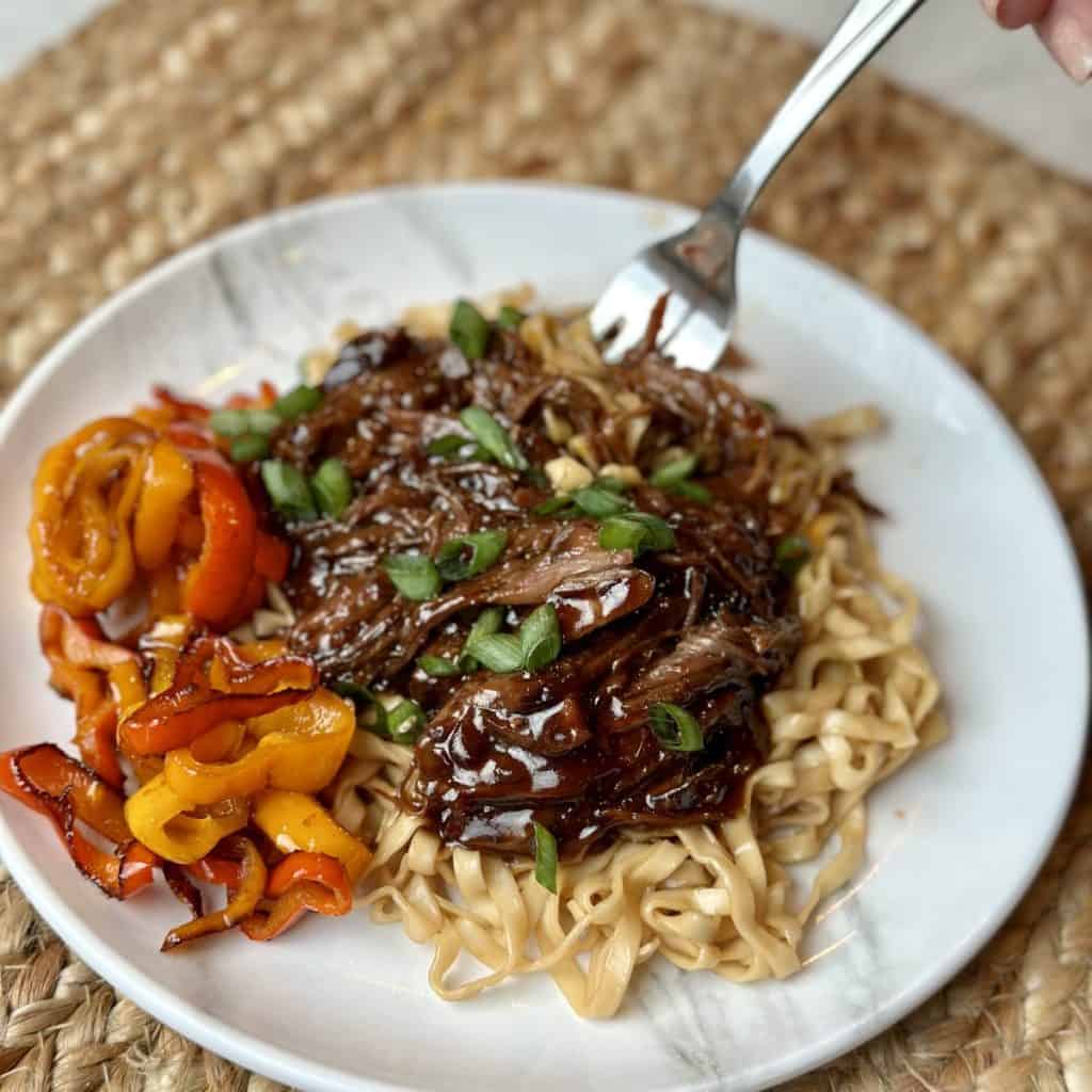 A plate of korean beef with noodles and vegetables.