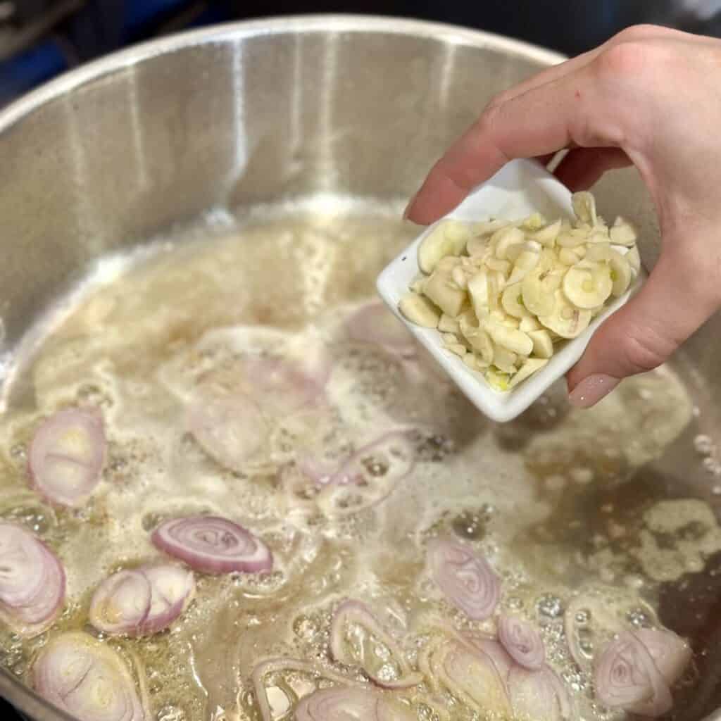 Adding garlic and shallots to a pan.