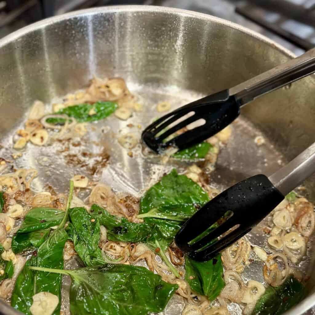 Mixing basil into broth in a pan.