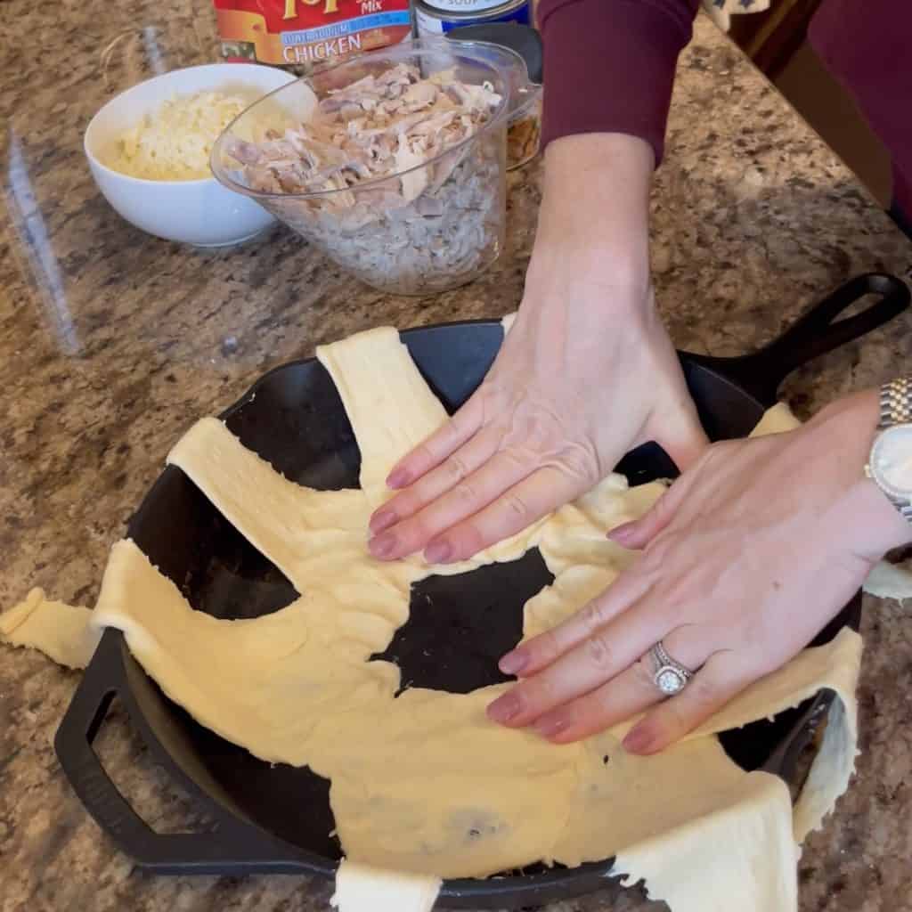 Pressing crescent rolls in a cast iron skillet.