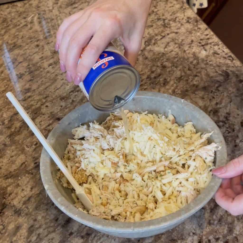 Adding broth to a bowl of chicken and stuffing.