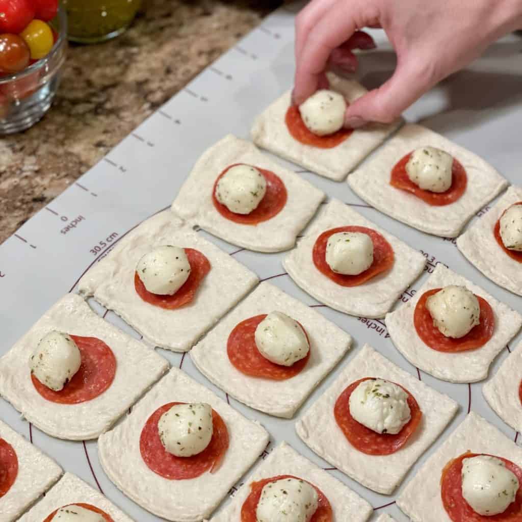 Laying mozzarella on pepperoni and pizza dough.