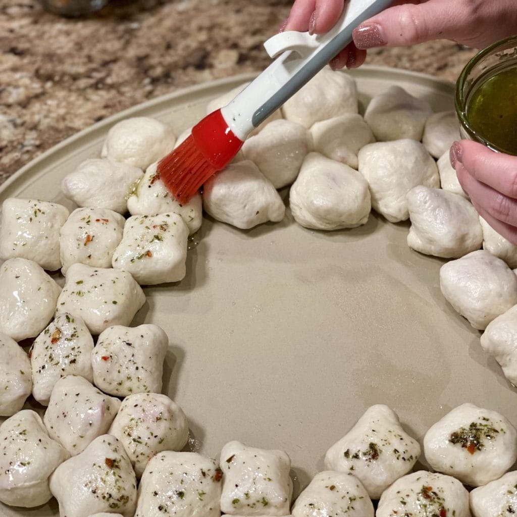 Brushing olive oil and seasoning on pizza rolls.