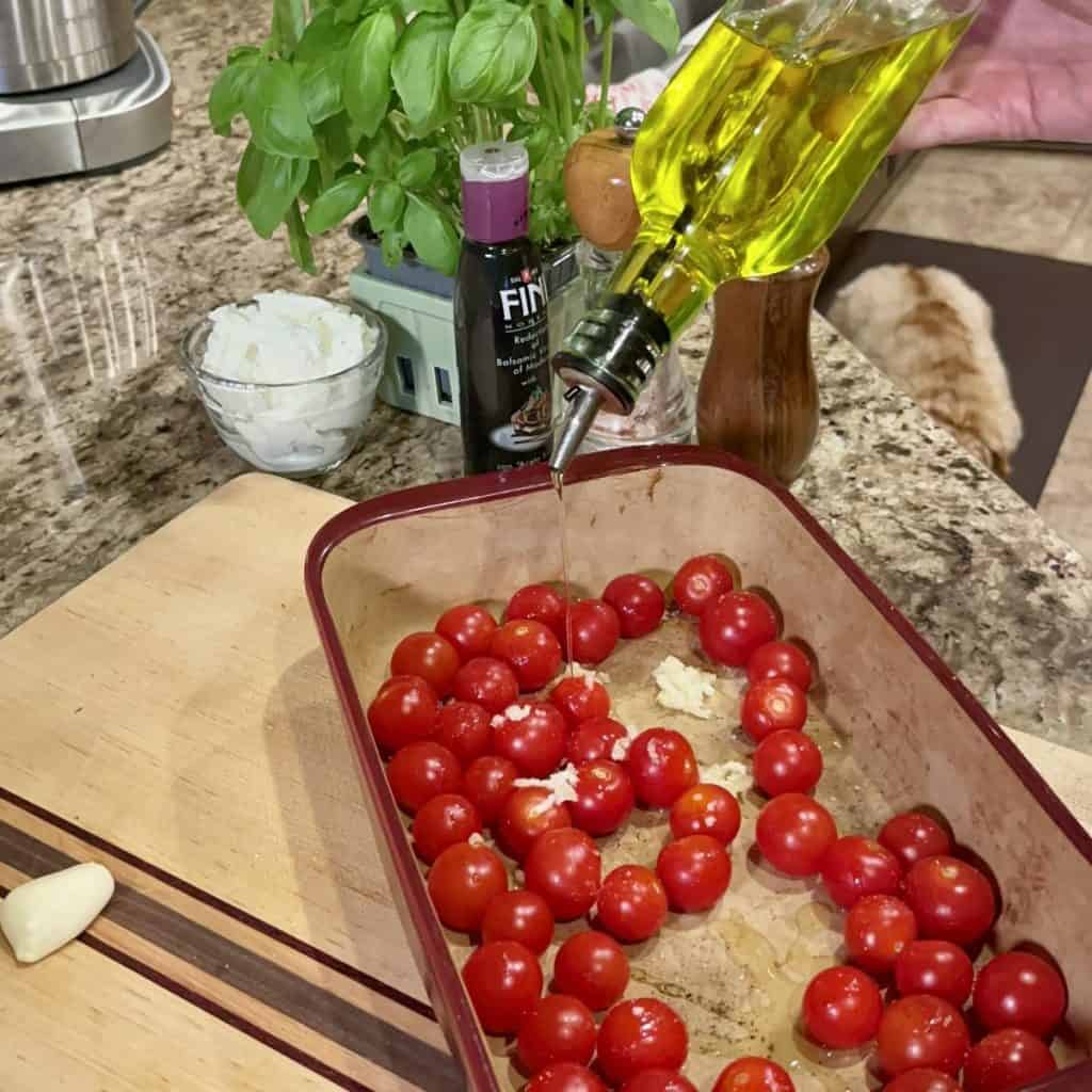 Mixing garlic, tomatoes and olive oil in a baking dish.