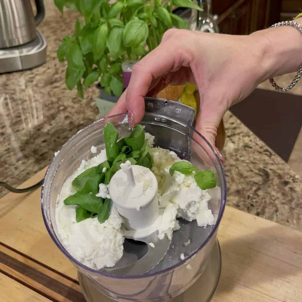 Mixing ricotta in a food processor with basil.