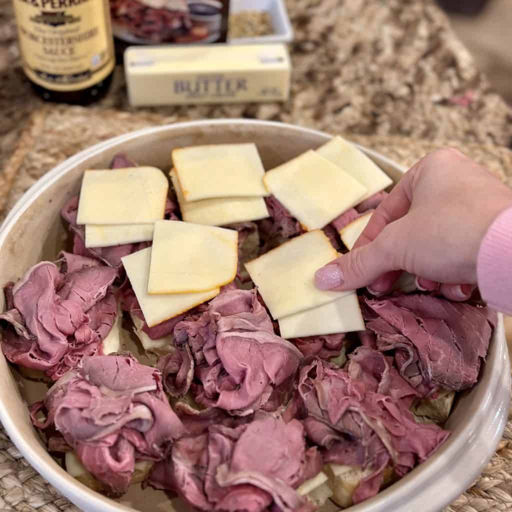 Adding cheese to beef sliders in a baking dish.