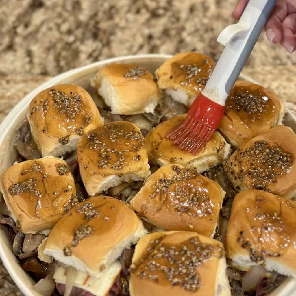 Brushing a seasoned butter mixture on top of sliders.