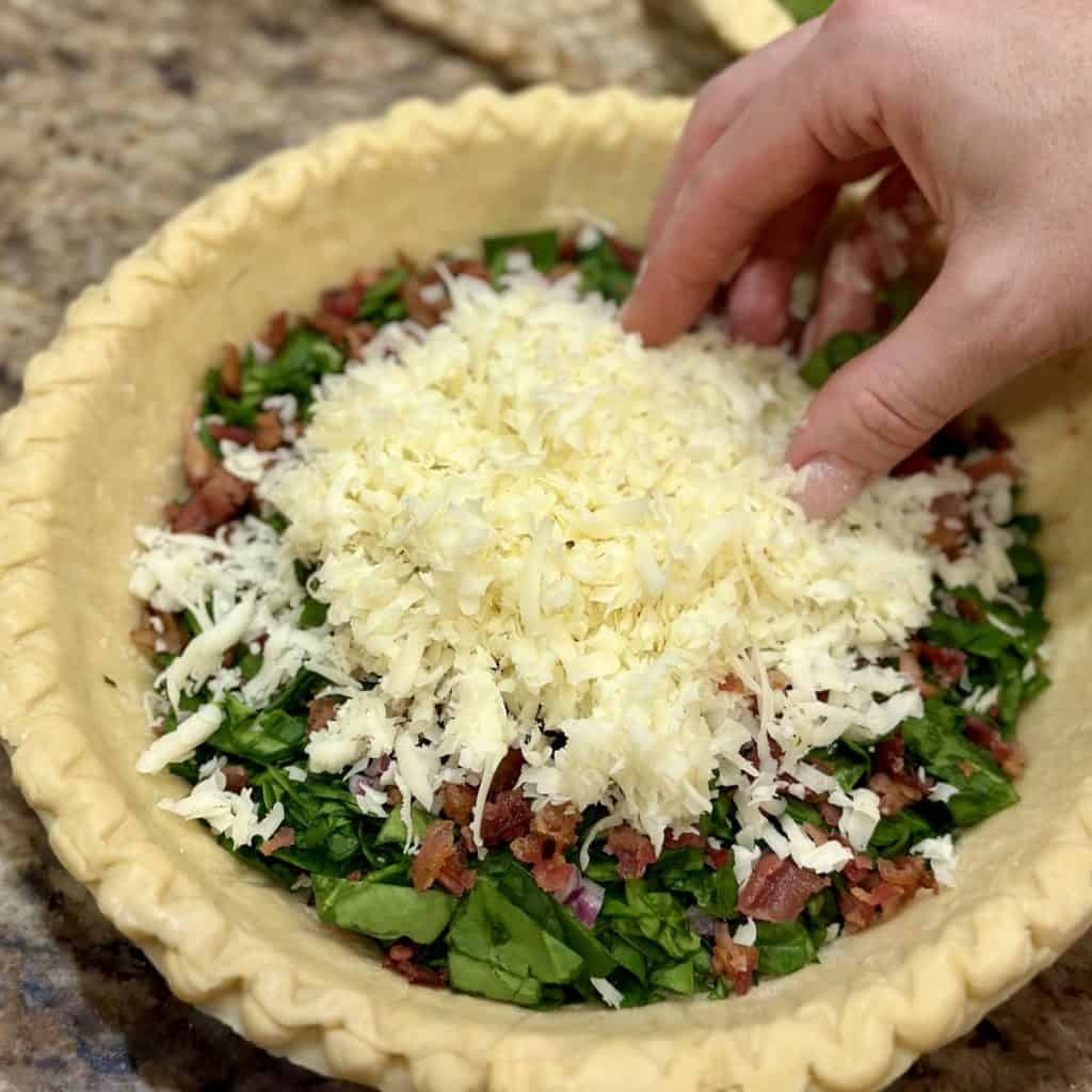 Adding cheese to the top of a quiche crust.