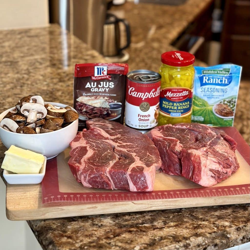 The ingredients to make a Mississippi french dip sandwich including roast, mushrooms, au jus packet, french onion soup, pepperoncini peppers, ranch seasoning and butter.