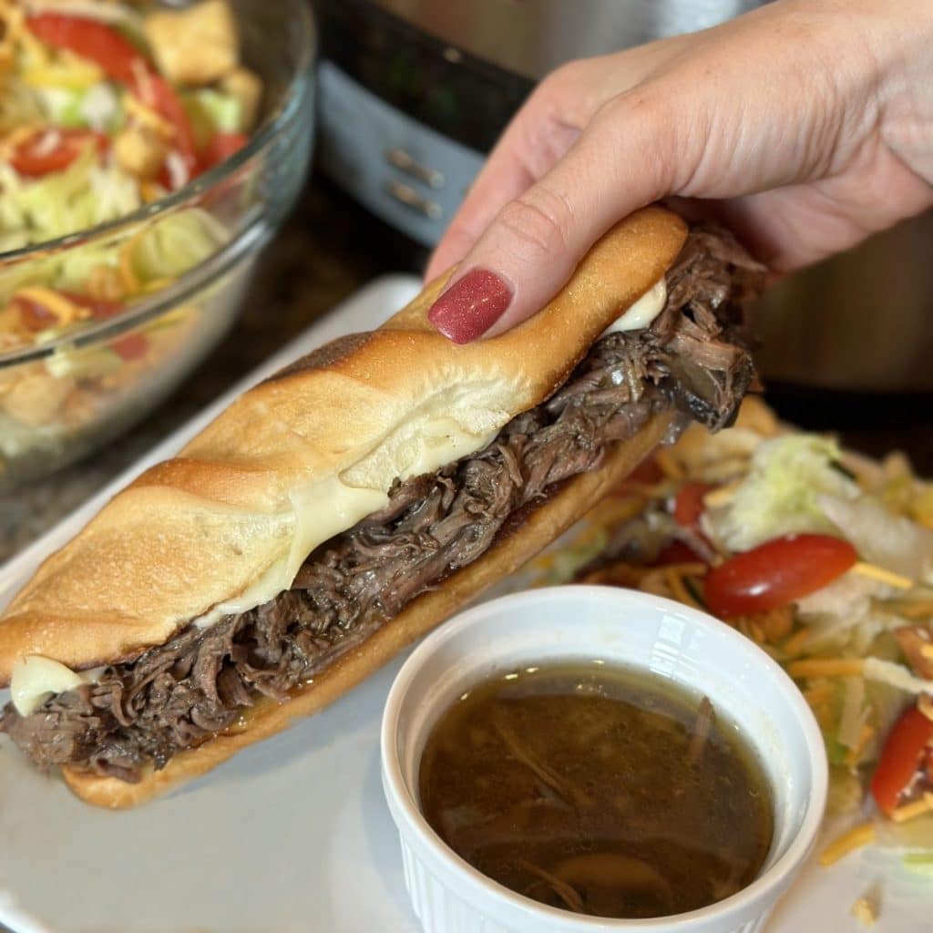 A beef sandwich with au jus dipping sauce on the side and a salad.