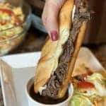 Beef sandwich being dipped in au jus broth.