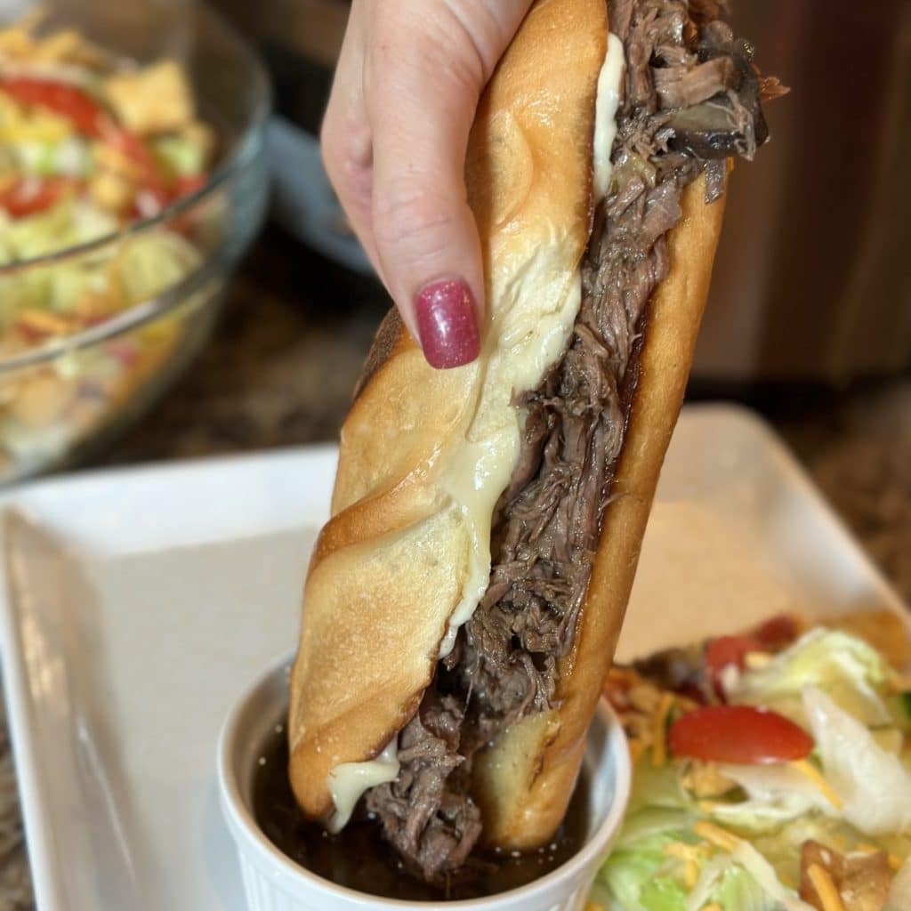 A beef sandwich being dipped in an au jus sauce.