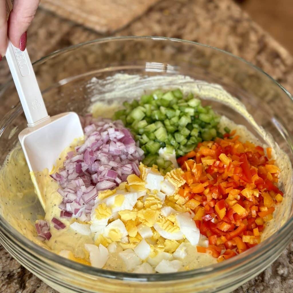 Macaroni salad ingredients in a bowl ready to be stirred including the dressing, vegetables and boiled egg.