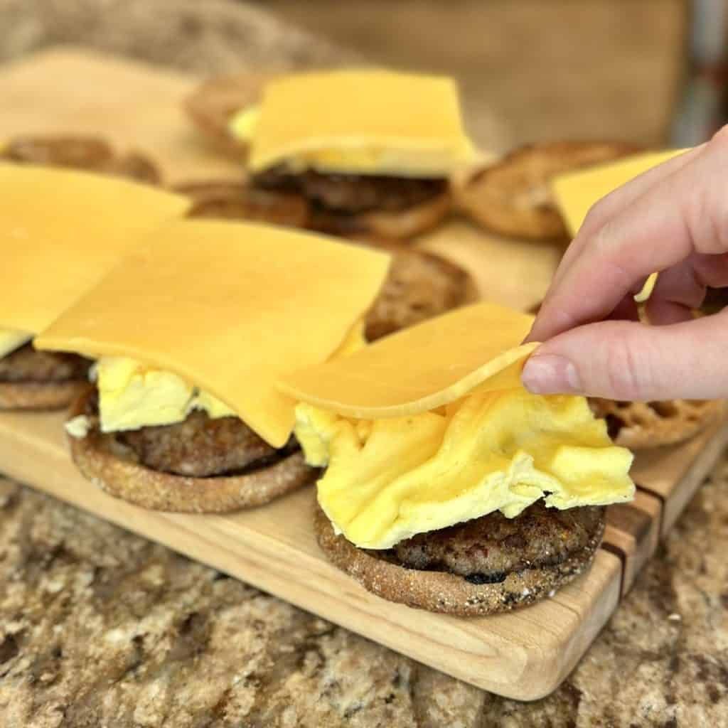 Adding cheese to the top of a breakfast sandwich.