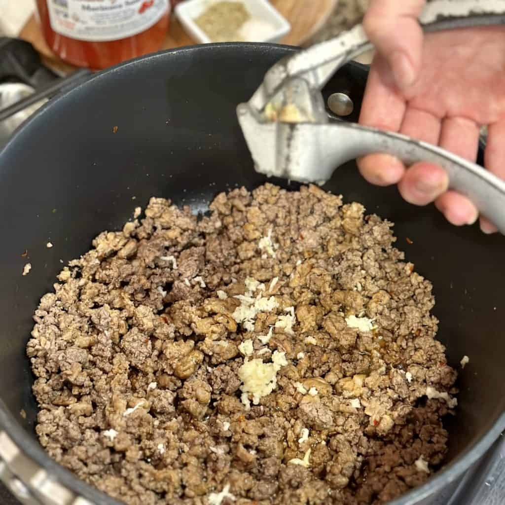Adding fresh garlic to a pot of beef and sausage.
