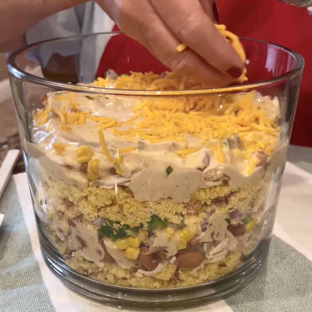 Adding cheese to the top of cornbread chicken salad.