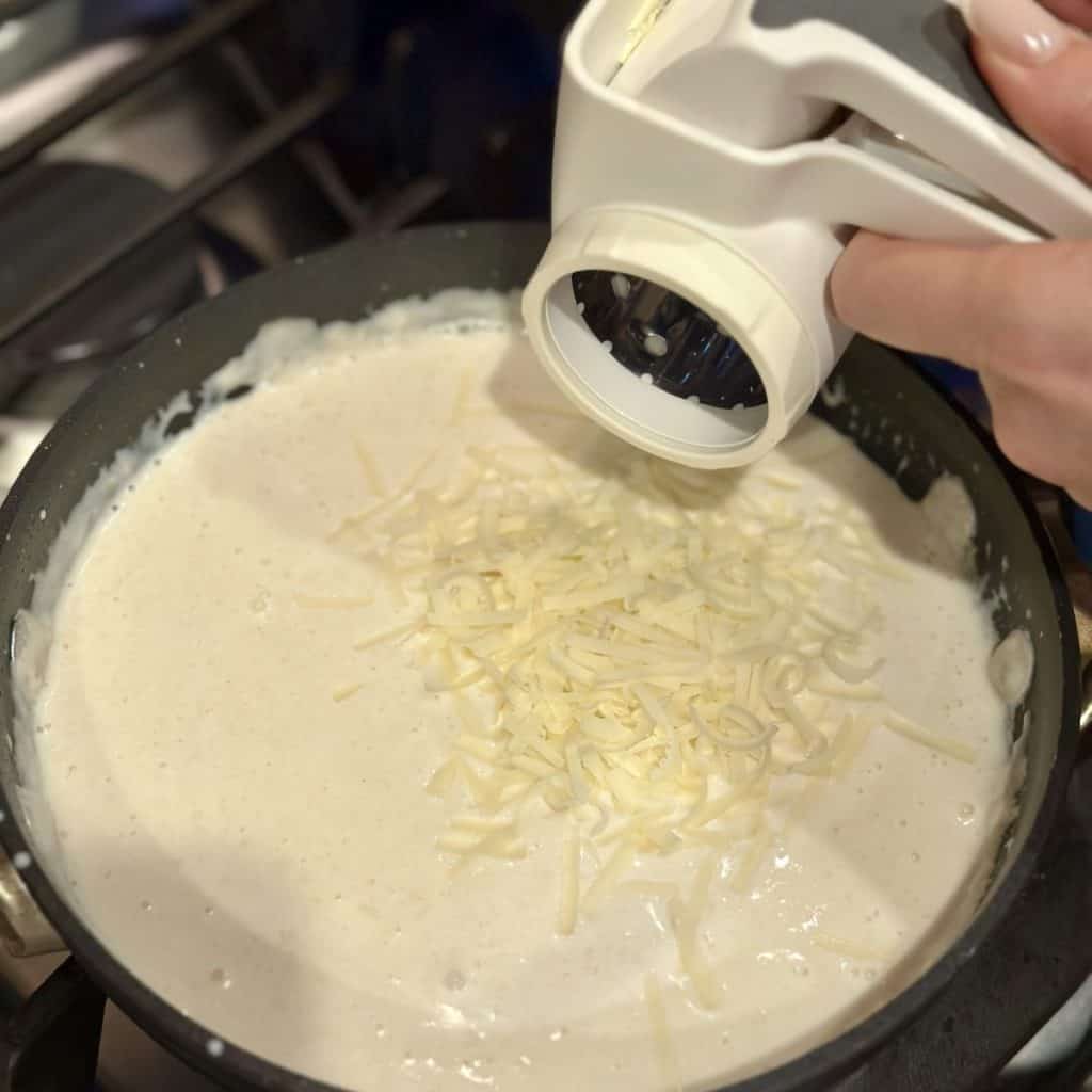 Adding parmesan cheese to milk in a pan.