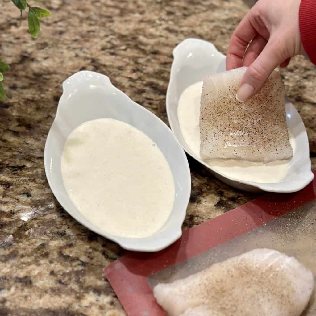 Laying cod filets in a cream sauce.