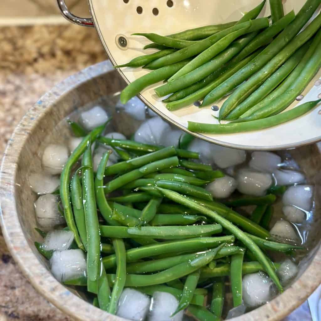 Adding blanched green beans to an ice bath.