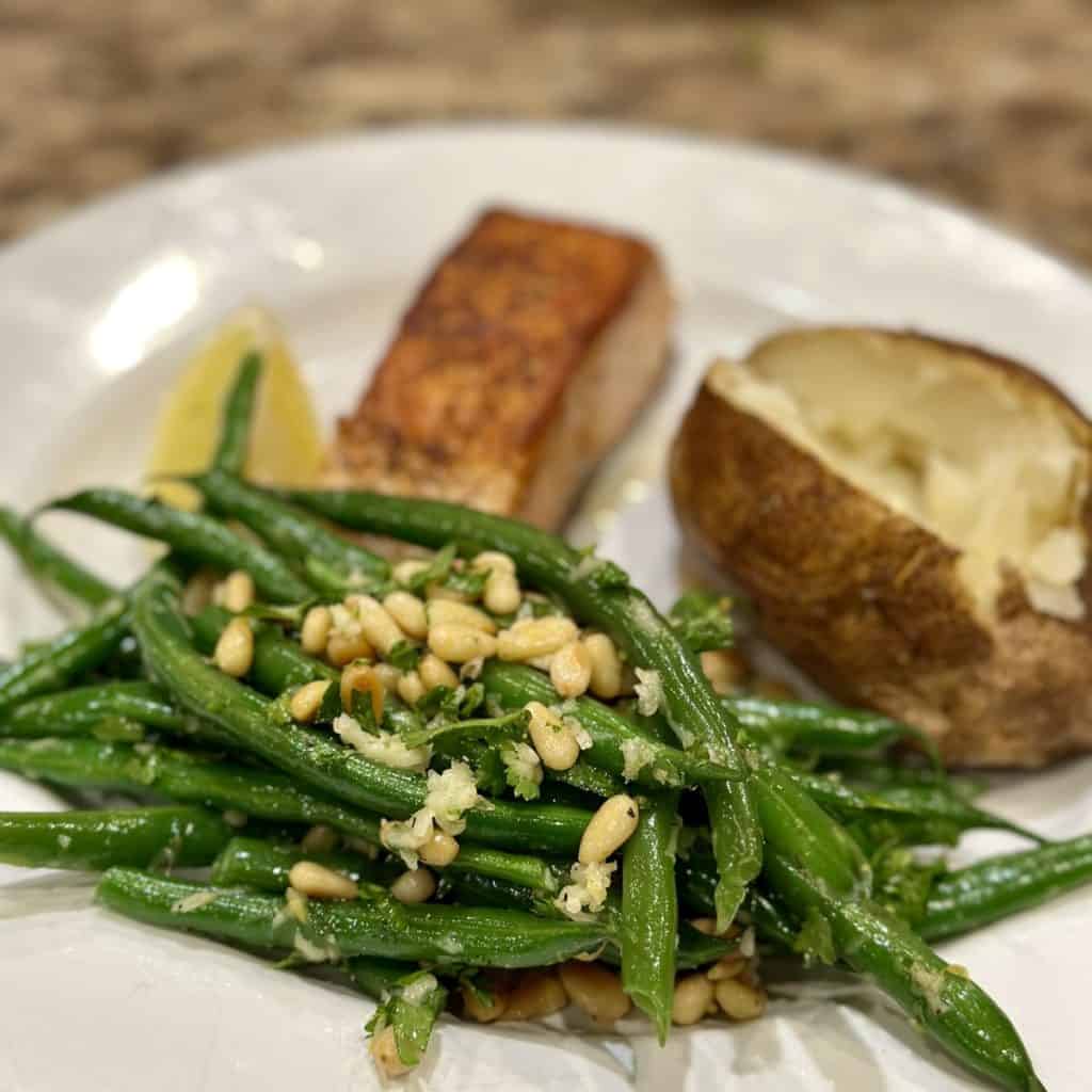 A plate of salmon, baked potato and gremolata green beans on a plate.